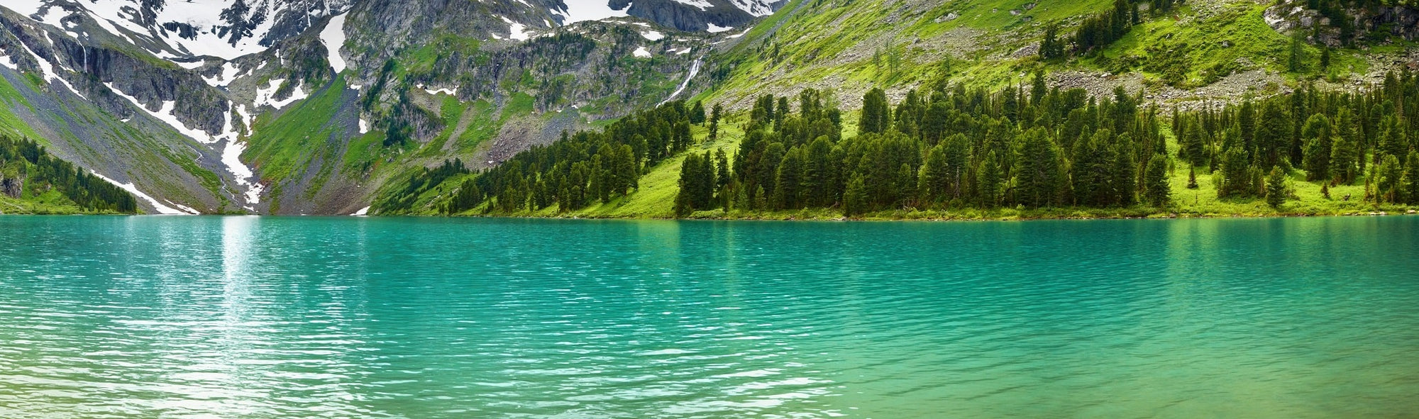 A crystal clear, green alpine lake is surrounded by snowy mountains, symbolic of our beautiful planet.