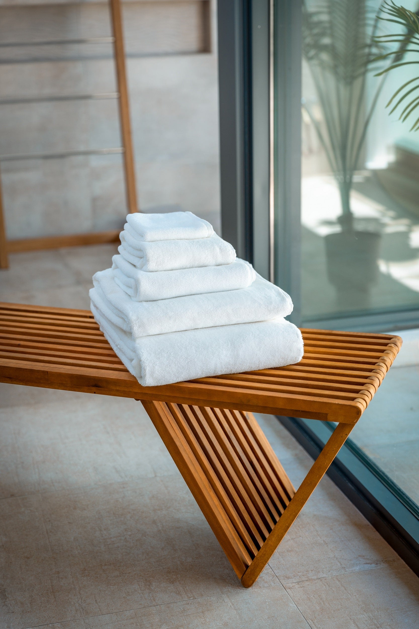 A stack of five different sizes of plush organic towels sits on a warm wooden bench.