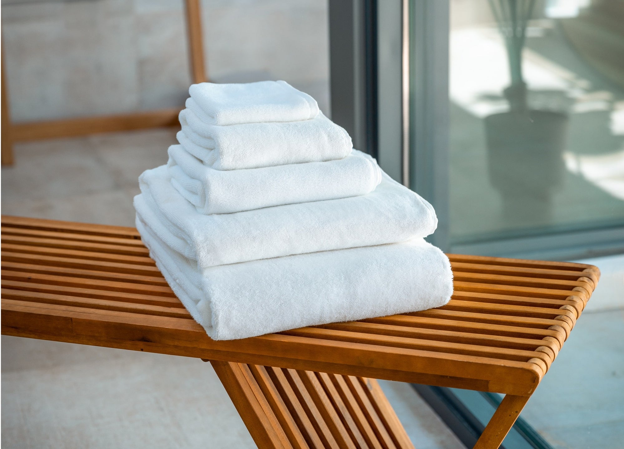 A stack of five different sizes of plush organic towels sits on a warm wooden bench.