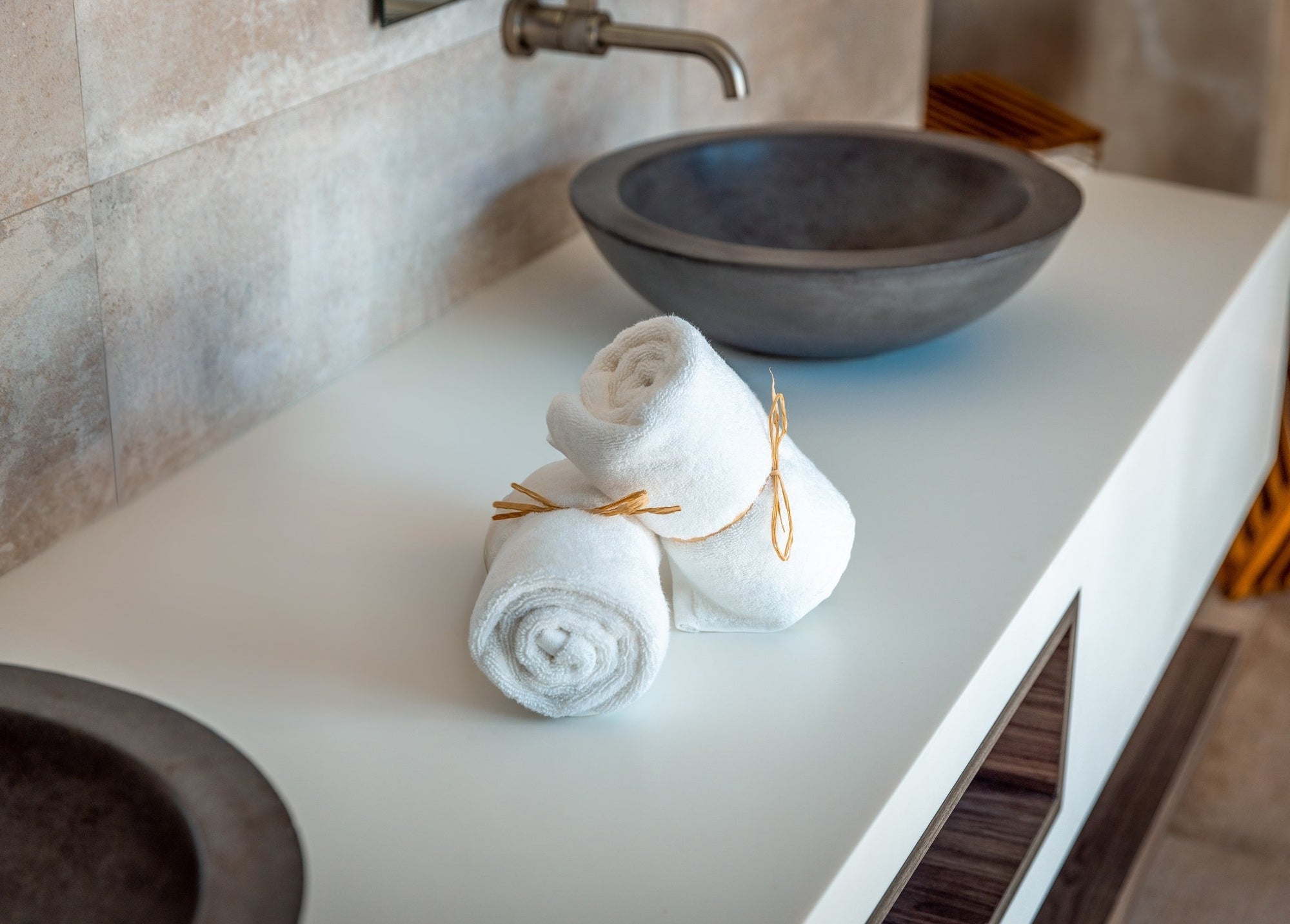 Two organic hand towels are rolled and tied on an eco-hotel bathroom countertop.