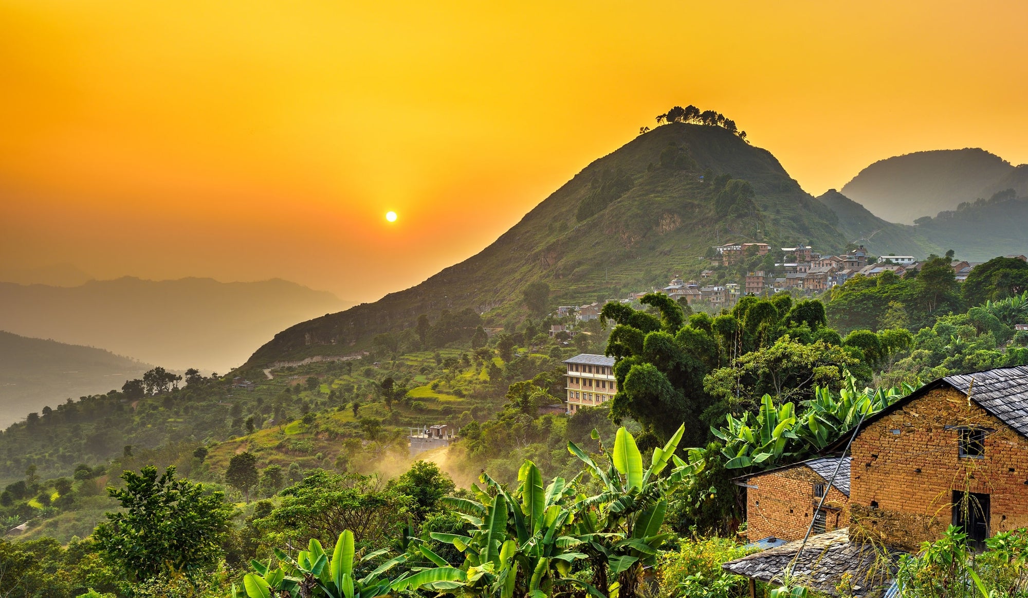 The sun sets over a beautiful town in Nepal overlooking a tropical area with reforestation projects underway.