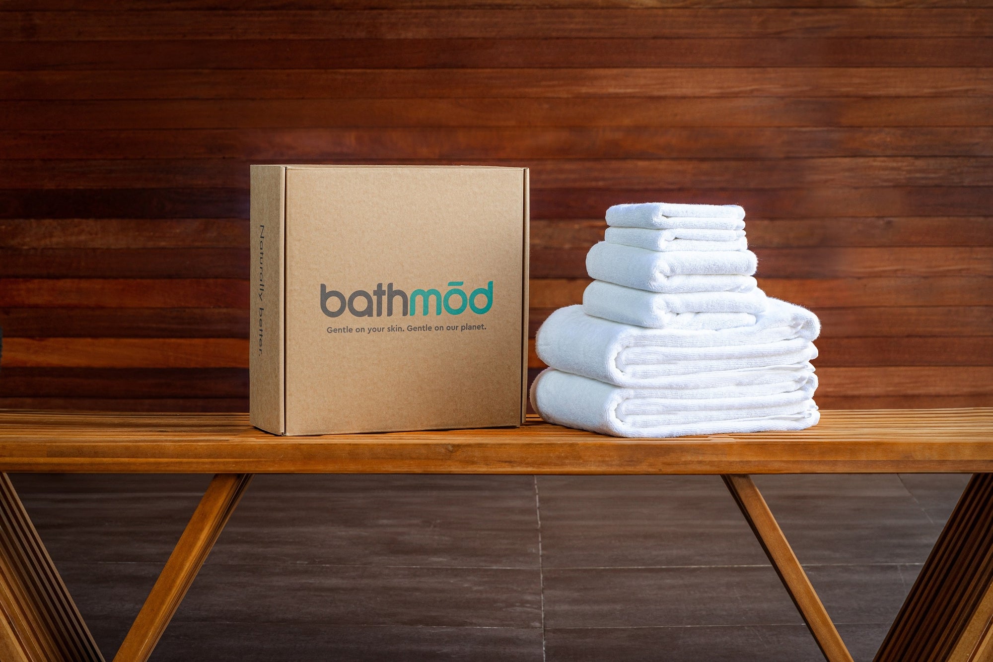 GOTS-certified organic towels are on a sustainable wooden bench next to eco-friendly packaging.