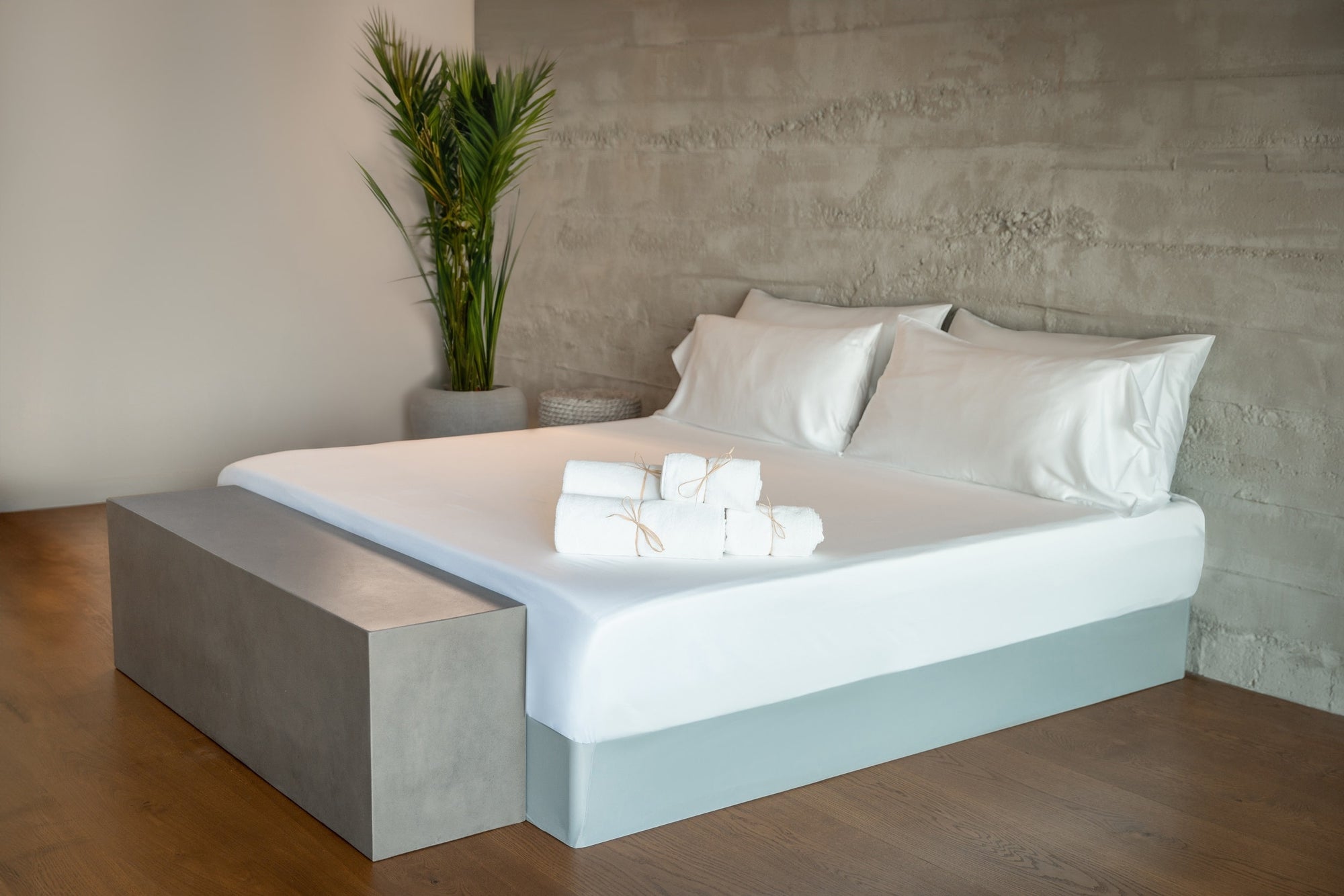 A perfectly made bed with freshly washed organic towels rolled up and tied, placed on the end of the bed.