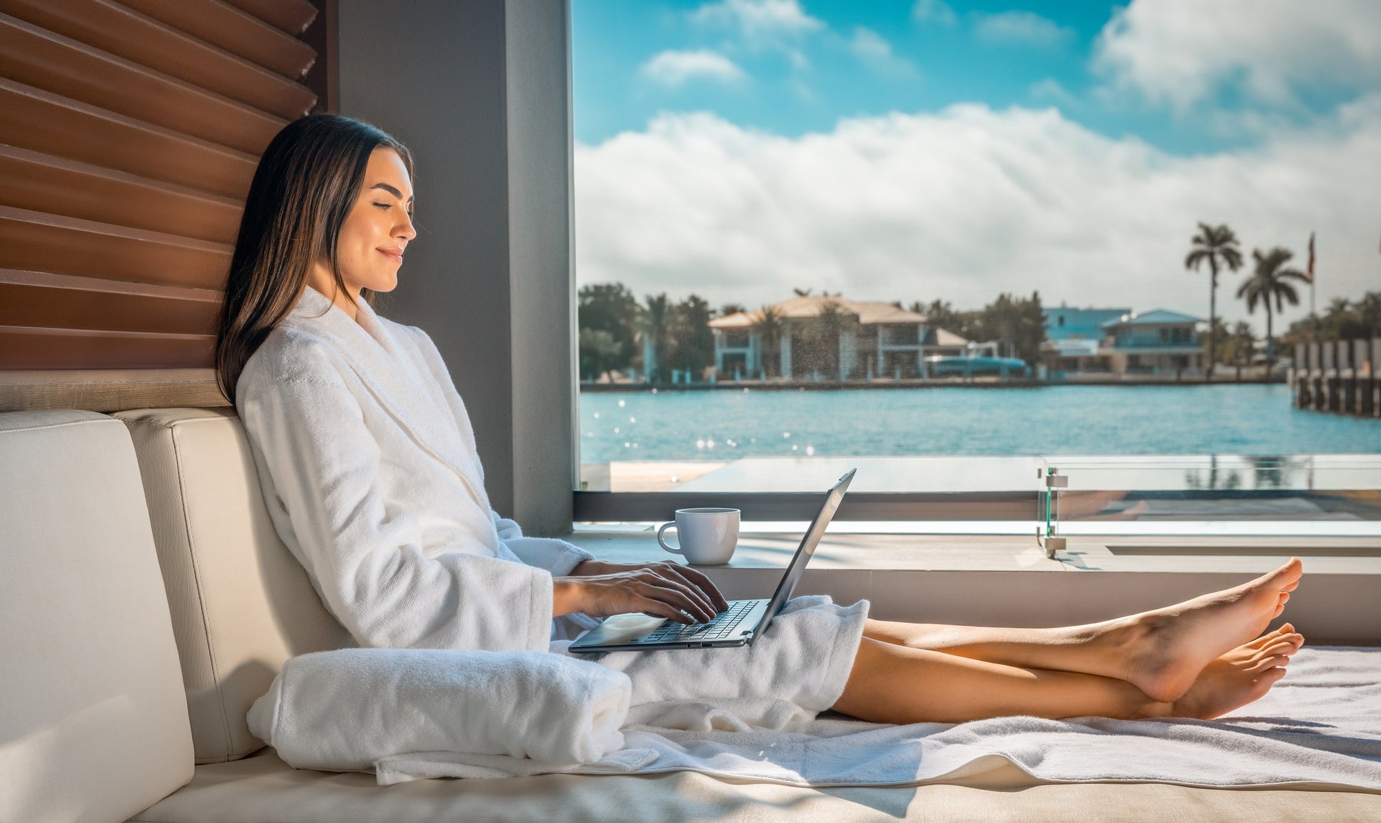 A woman in an organic white bath robe is sitting by the pool in a modern sustainable home.